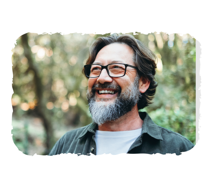 Ein Mann steht lächelnd in einem Wald.