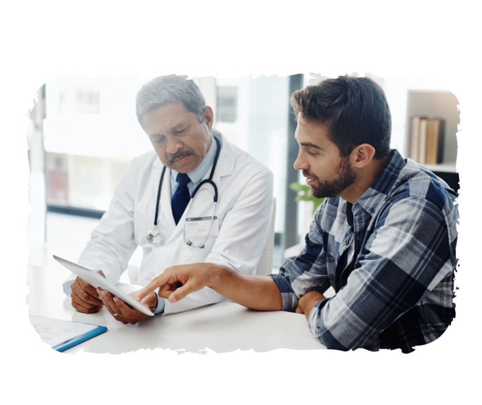 Ein Arzt und ein weiterer Mann sitzen an einem Tisch, beide schauen auf einen Tablet-Computer.