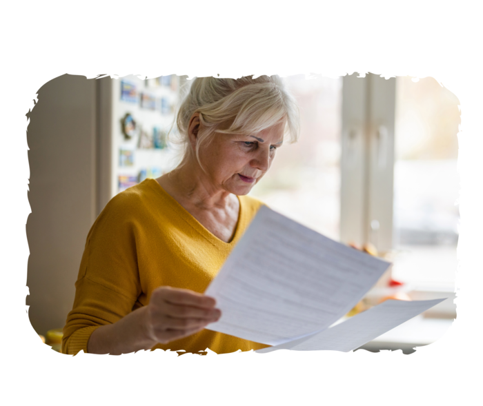 Eine ältere Frau schaut auf zwei bedruckte Blätter Papier, die sie in ihren Händen hält.