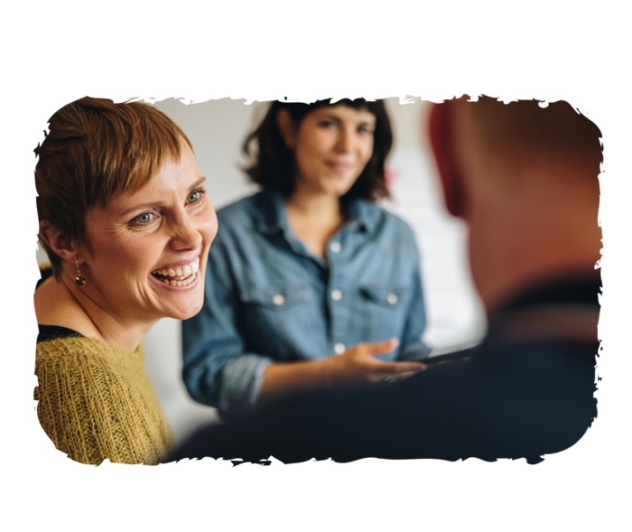 Zwei Frauen und ein Mann sitzen sich gegenüber. Eine der Frauen lacht.