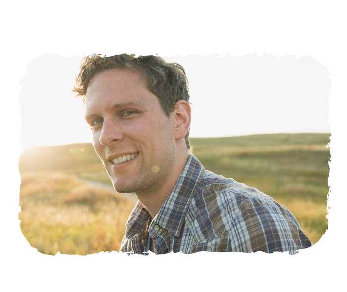 Ein Mann steht vor einem Feld und lächelt in die Kamera.