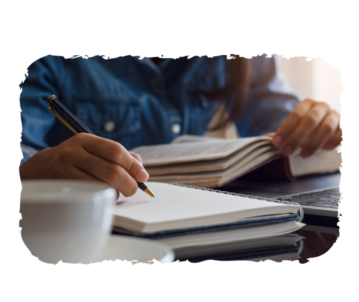 Eine Person schreibt auf einen Notizblock, der neben einem Laptop liegt. 