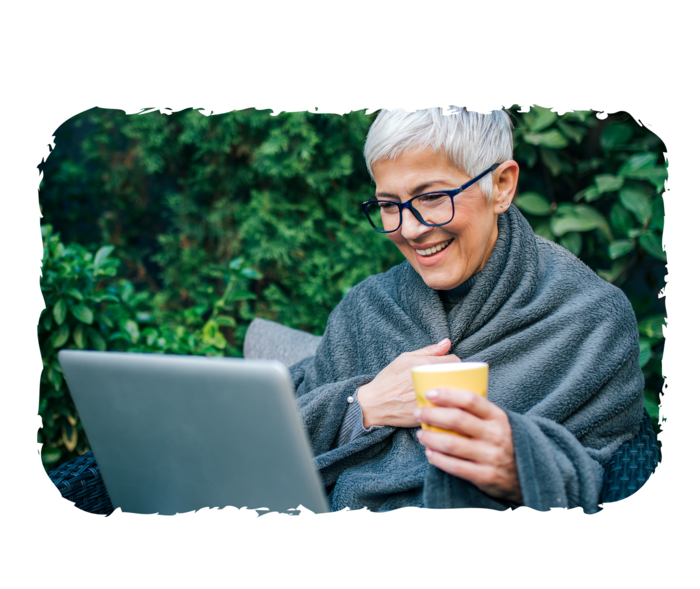 Eine ältere Frau sitzt draußen und schaut auf einen Laptop auf ihrem Schoß.