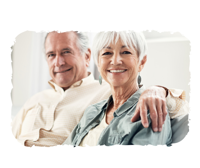 Myeloproliferative Neoplasien Eine ältere Frau und ein älterer Mann sitzen zusammen auf dem Sofa und lächeln in die Kamera.