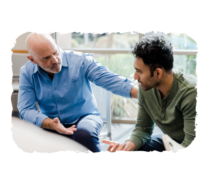 Ein älterer Mann fasst einem jüngeren Mann auf die Schulter und schaut ihn an.