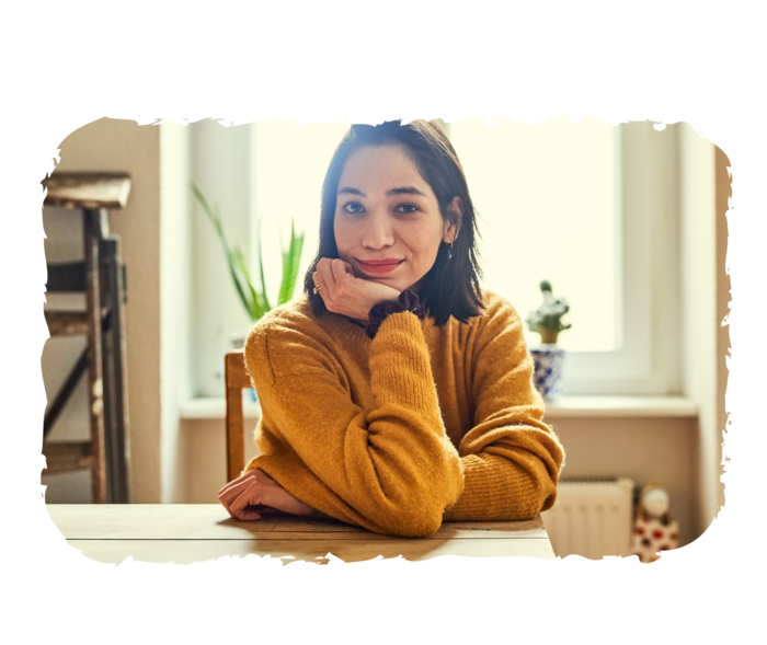 Eine Frau sitzt an einem Tisch und schaut in die Kamera.