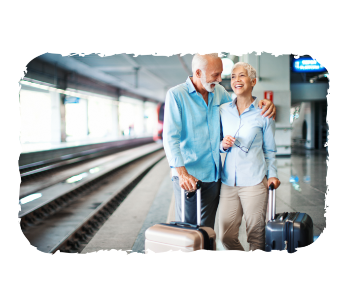 Ein älterer Mann und eine ältere Frau stehen mit zwei Koffern an einem Bahnsteig.