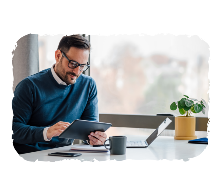 Ein Mann sitzt an einem Schreibtisch und schaut auf ein Tablet.