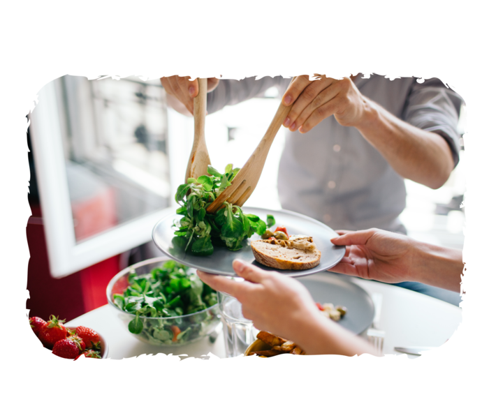Leben mit PNH: Ernährung Ein Mann hält zwei Holzlöffel und legt Salat auf einen Teller ab.