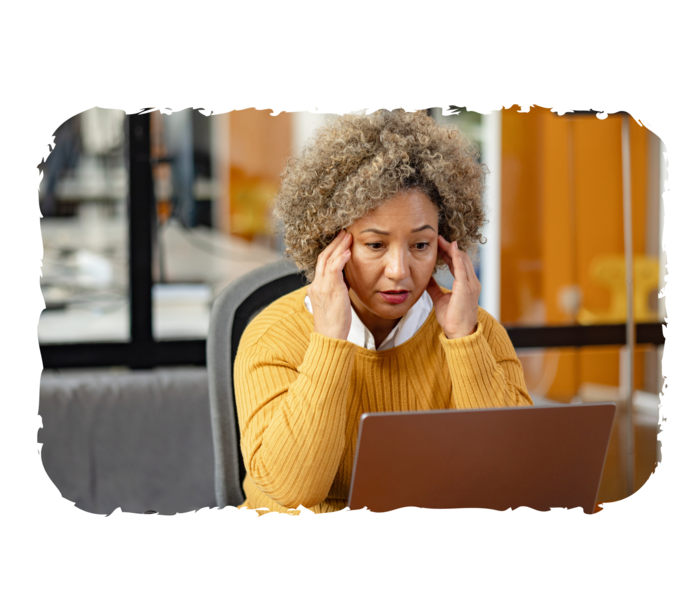 PNH: Fatigue Eine Person sitzt vor einem Laptop und fasst sich an die Schläfen.