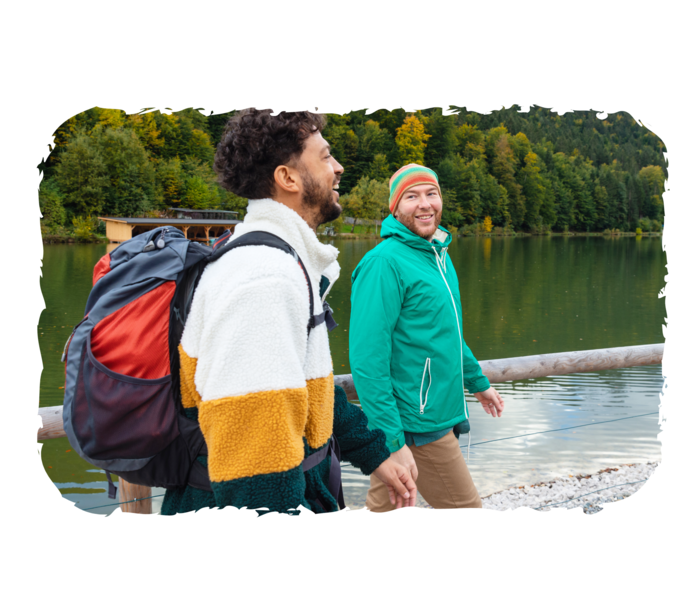 Zwei Personen gehen an einem Gewässer entlang und lächeln.  