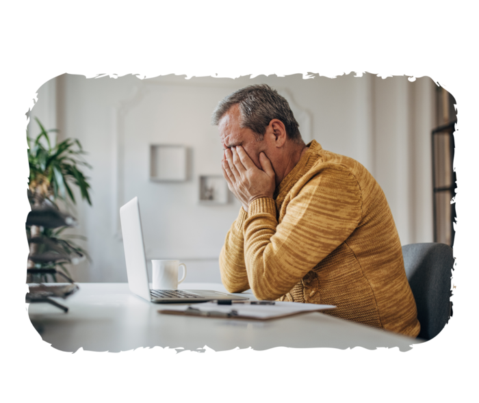 Eine Person sitzt vor einem Laptop und stützt den Kopf in die Hände. 