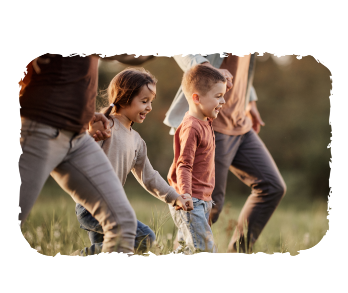 Zwei kleine Kinder und zwei Erwachsene halten sich an den Händen und laufen über eine Wiese.