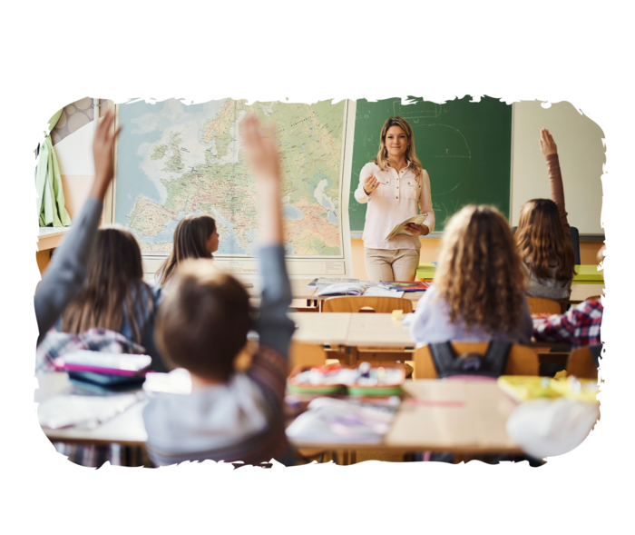 Eine Lehrerin steht vor einer Schulklasse. Einige der Kinder heben den Arm.