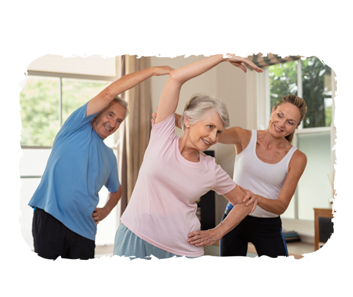 Eine Frau und ein Mann im Seniorenalter werden von einer Trainerin bei gymnastischen Übungen unterstützt. 