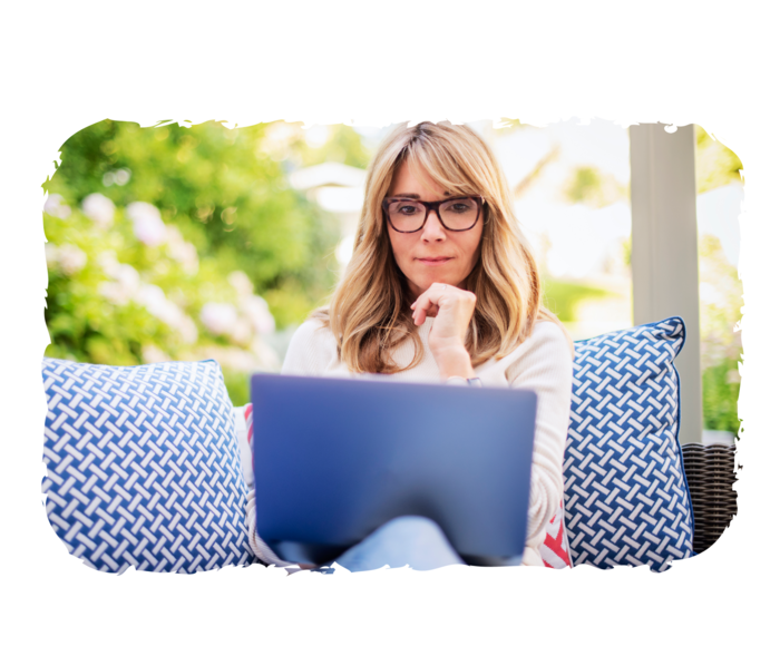 Eine ältere Person sitzt auf einer Sitzgelegenheit und betrachtet den Laptop auf ihrem Schoß.