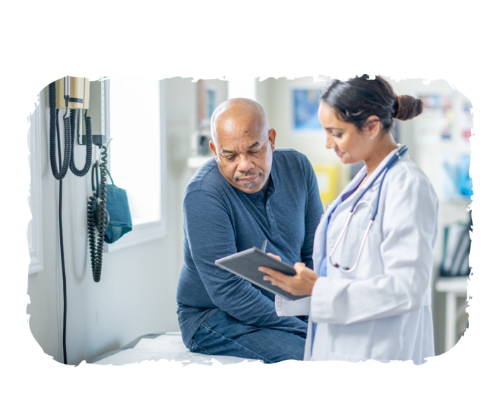 Eine ältere Person sitzt auf einer Liege, während eine andere Person in weißem Kittel ihr etwas auf einem Klemmbrett zeigt. 