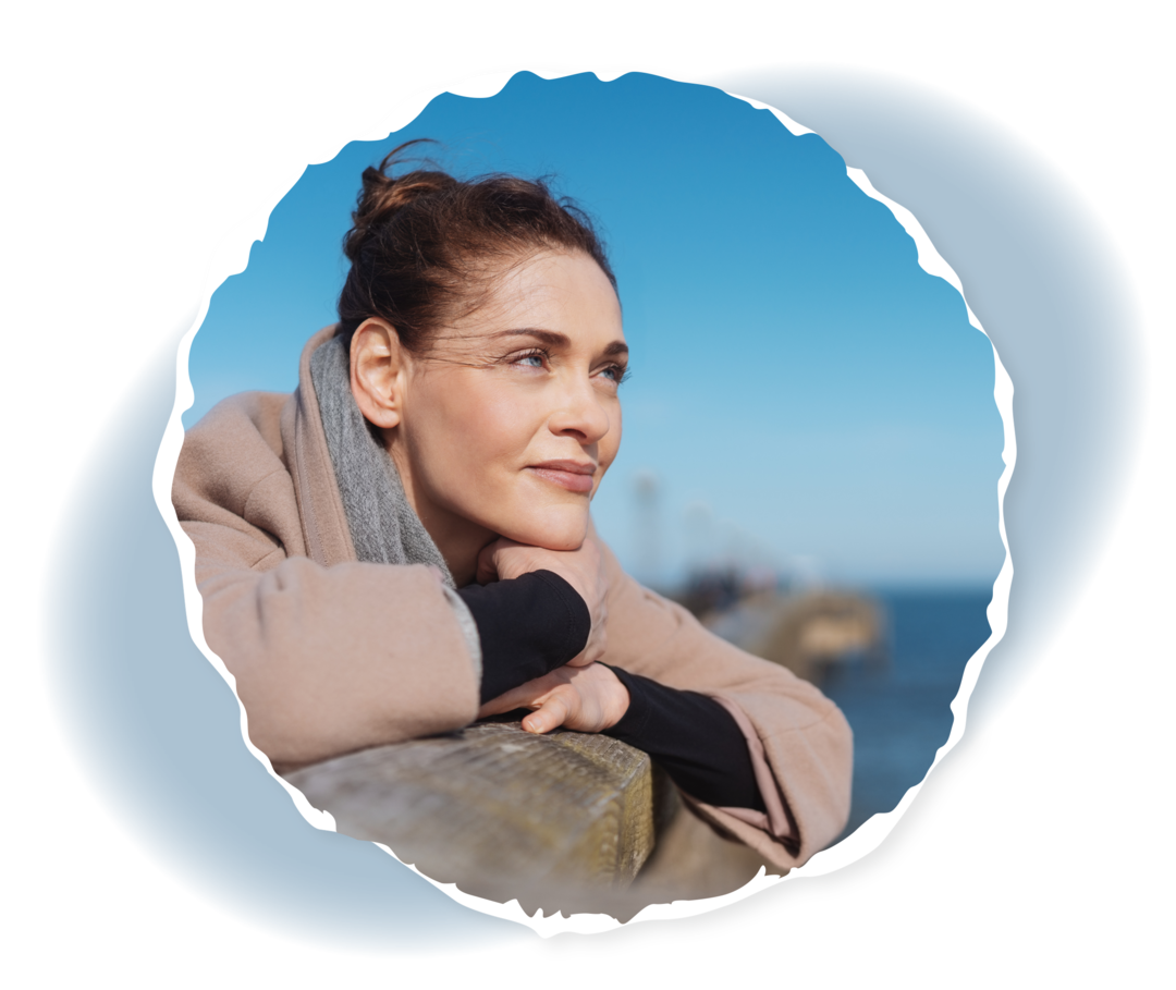 Frau lehnt sich an ein Geländer und schaut auf ein Gewässer.