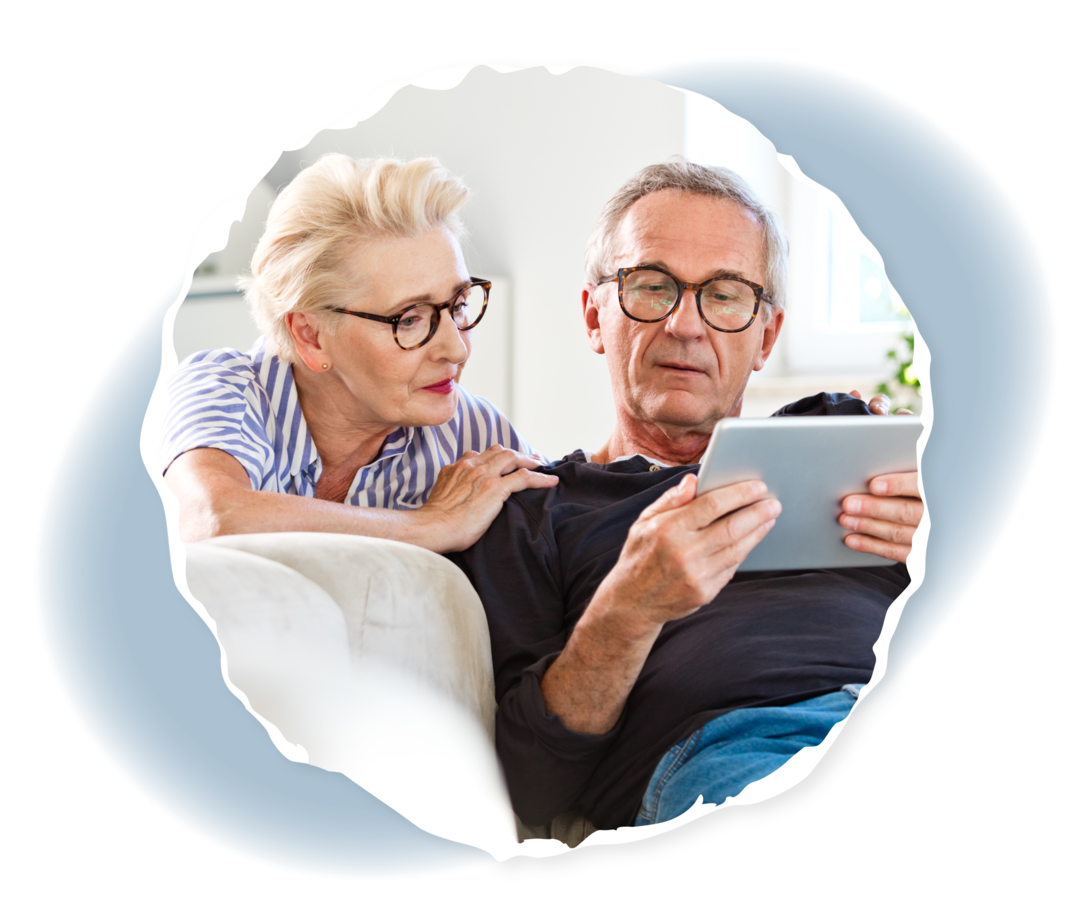 Selbstfürsorge für Angehörige: Überforderung entgegenwirken Eine Frau und ein Mann sitzen auf einem Sofa und schauen auf einen Tablet-Computer.