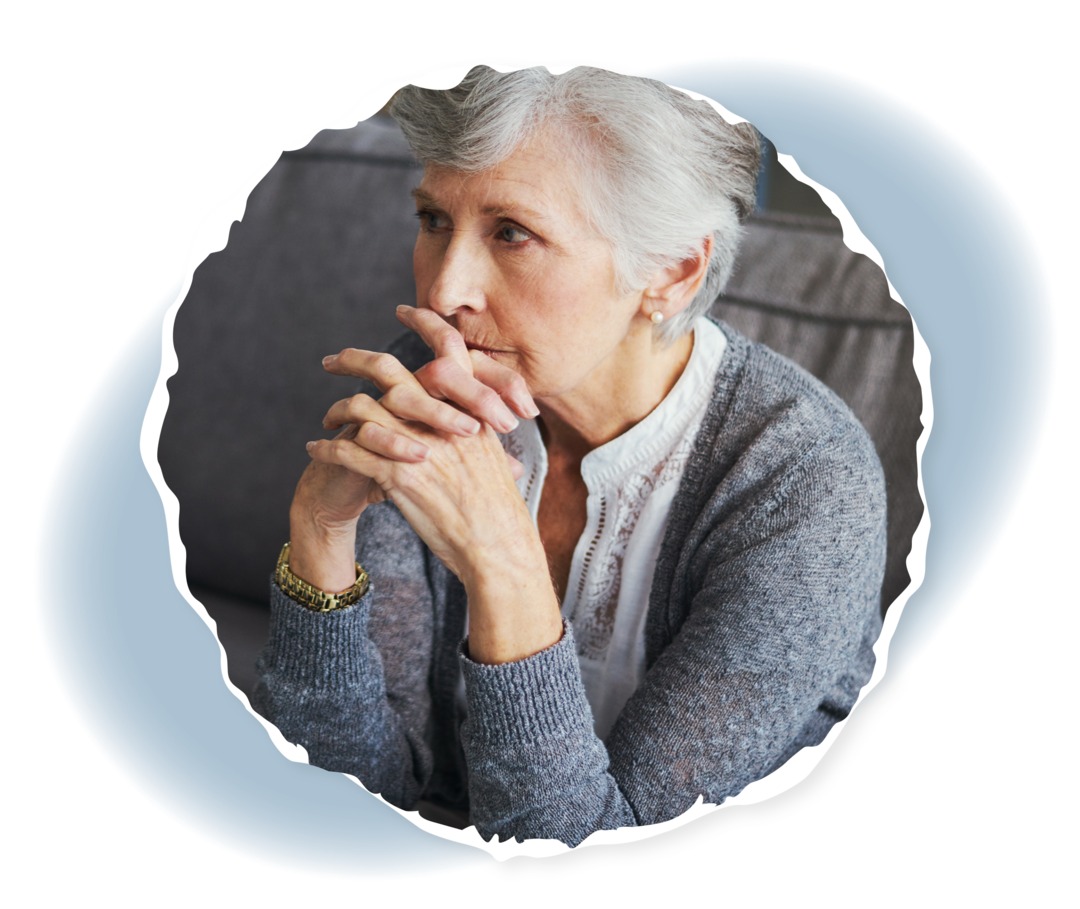 Eine Frau sitzt mit gefalteten Händen vor dem Mund auf einem Sofa.