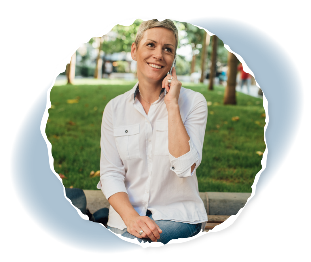 Eine Frau sitzt auf einer Bank im Freien und hält ein Smartphone an ihr Ohr.