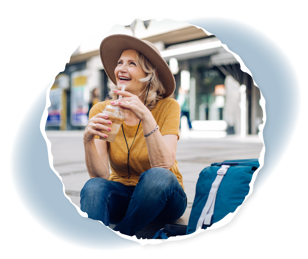 Frau sitzt mit einem Getränk in der Hand draußen und trägt einen Sonnenhut.