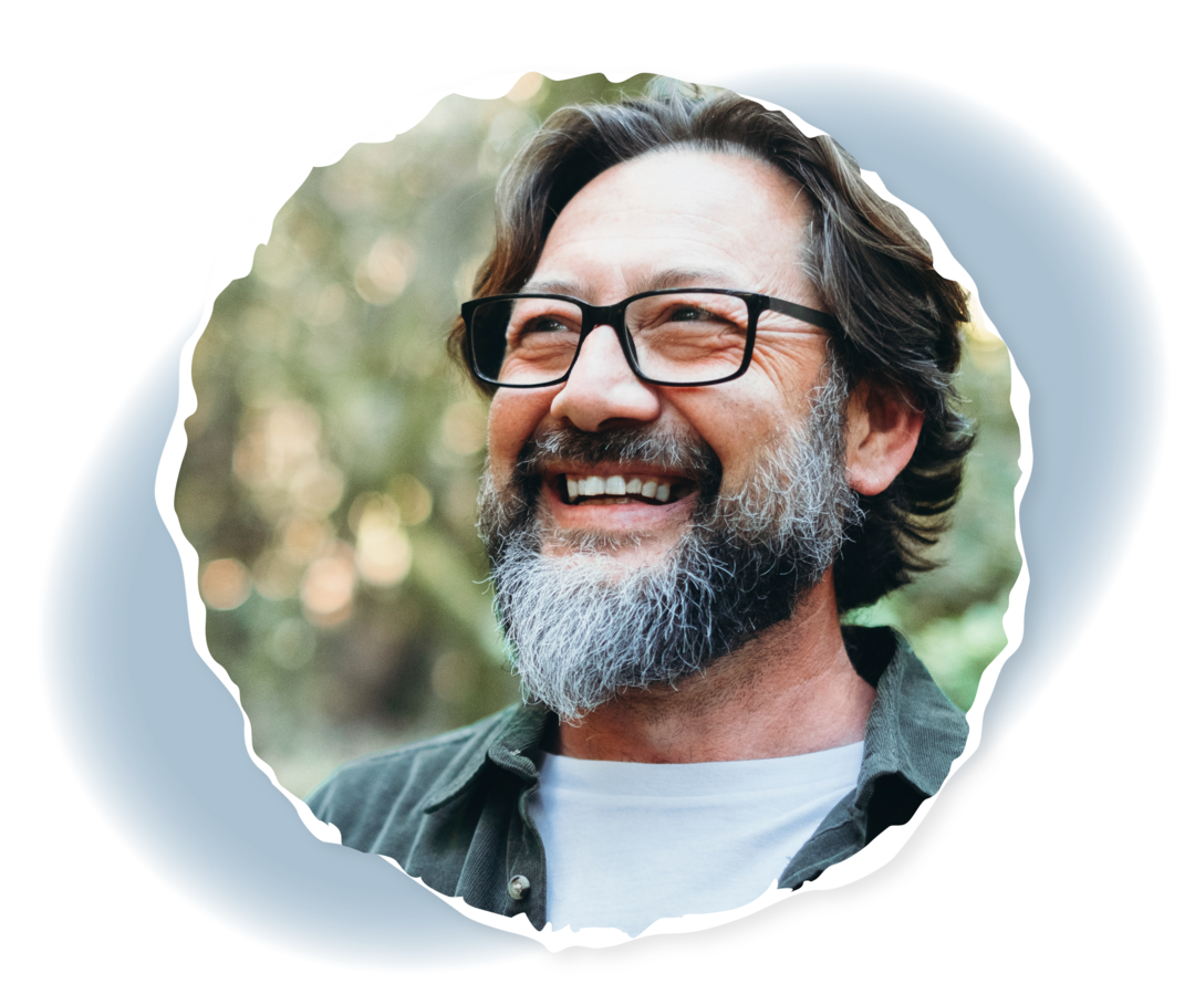 Für Angehörige: Selbstfürsorge Ein Mann steht lächelnd in einem Wald.