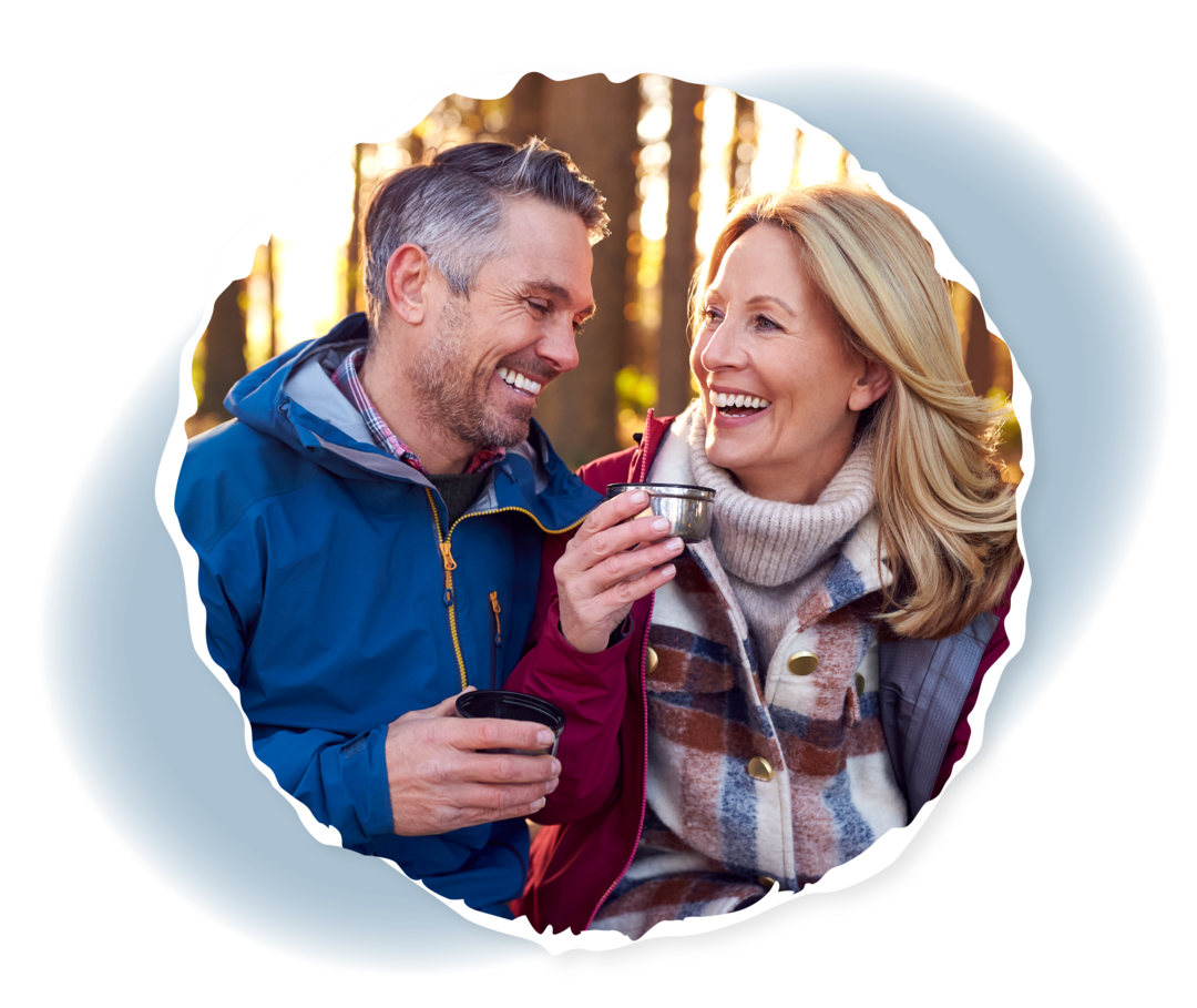 Ein Mann und ein Frau sitzen lachend in einem Wald.