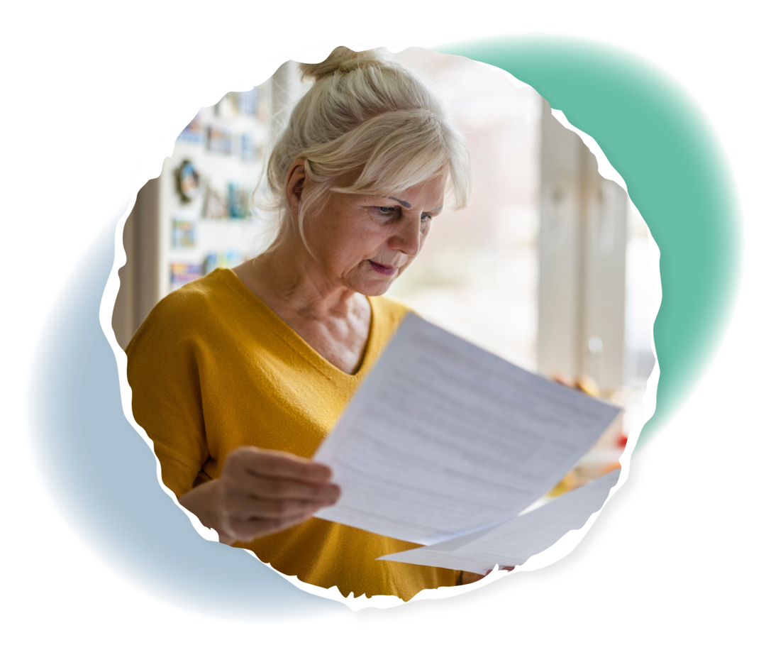 Eine ältere Frau schaut auf zwei bedruckte Blätter Papier, die sie in ihren Händen hält.