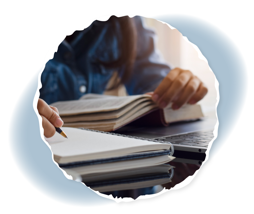 Eine Person schreibt auf einen Notizblock, der neben einem Laptop liegt.