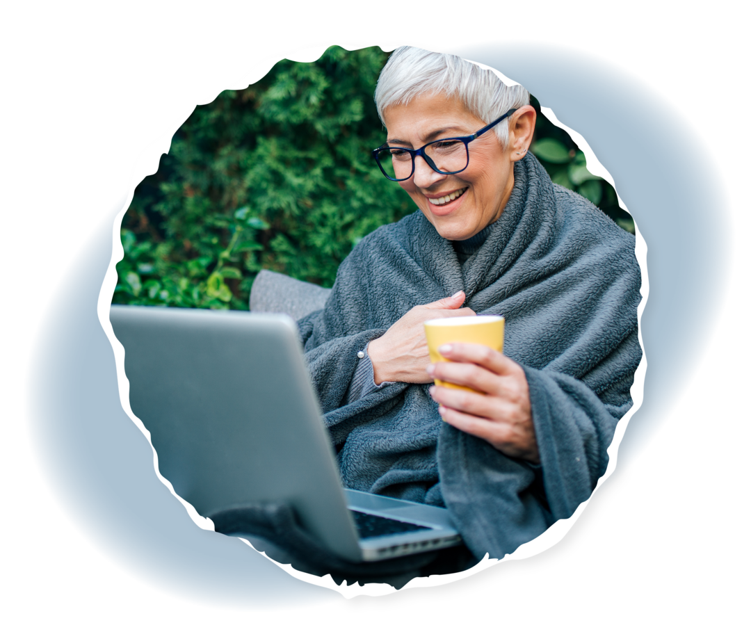 Eine ältere Frau sitzt draußen und schaut auf einen Laptop auf ihrem Schoß.