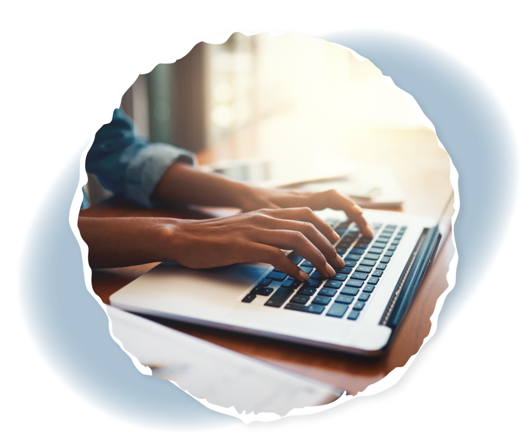 Nahaufnahme zweier Hände auf einer Laptop-Tastatur. Daneben ein Notizbuch.