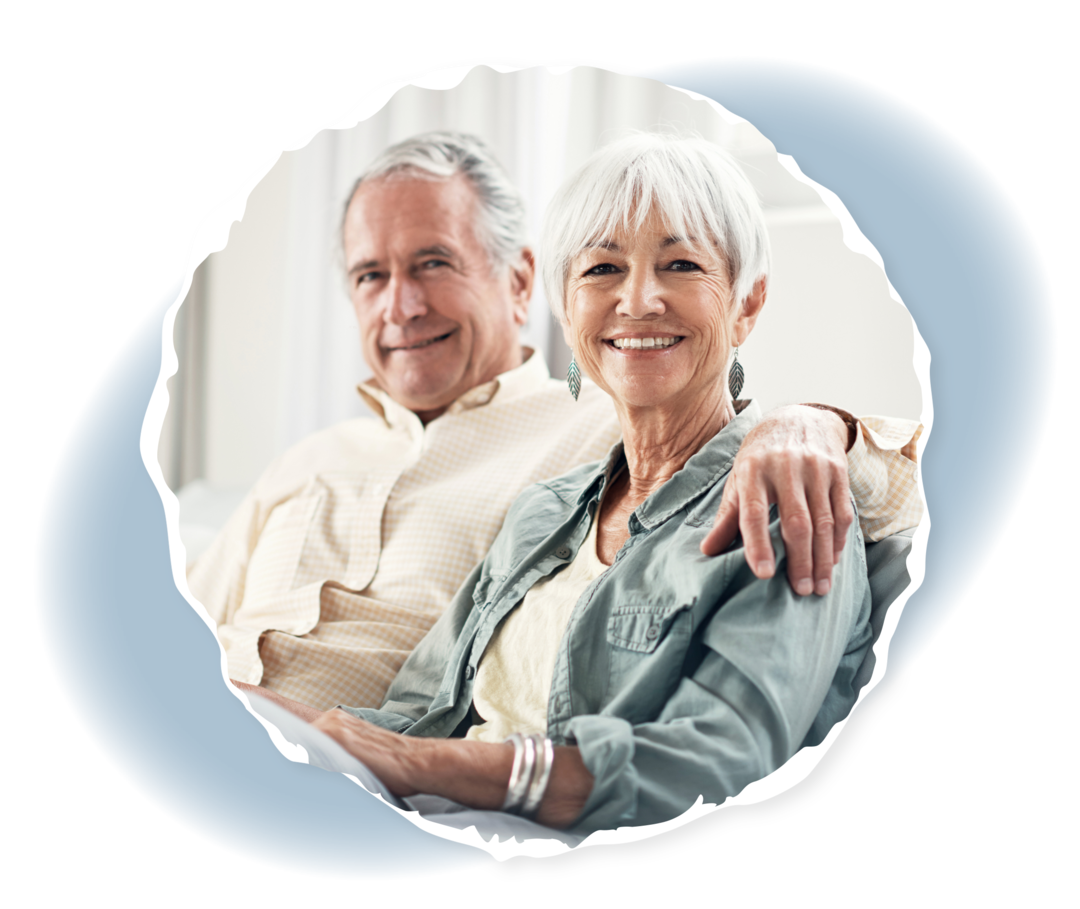 Myeloproliferative Neoplasien Eine ältere Frau und ein älterer Mann sitzen zusammen auf dem Sofa und lächeln in die Kamera.
