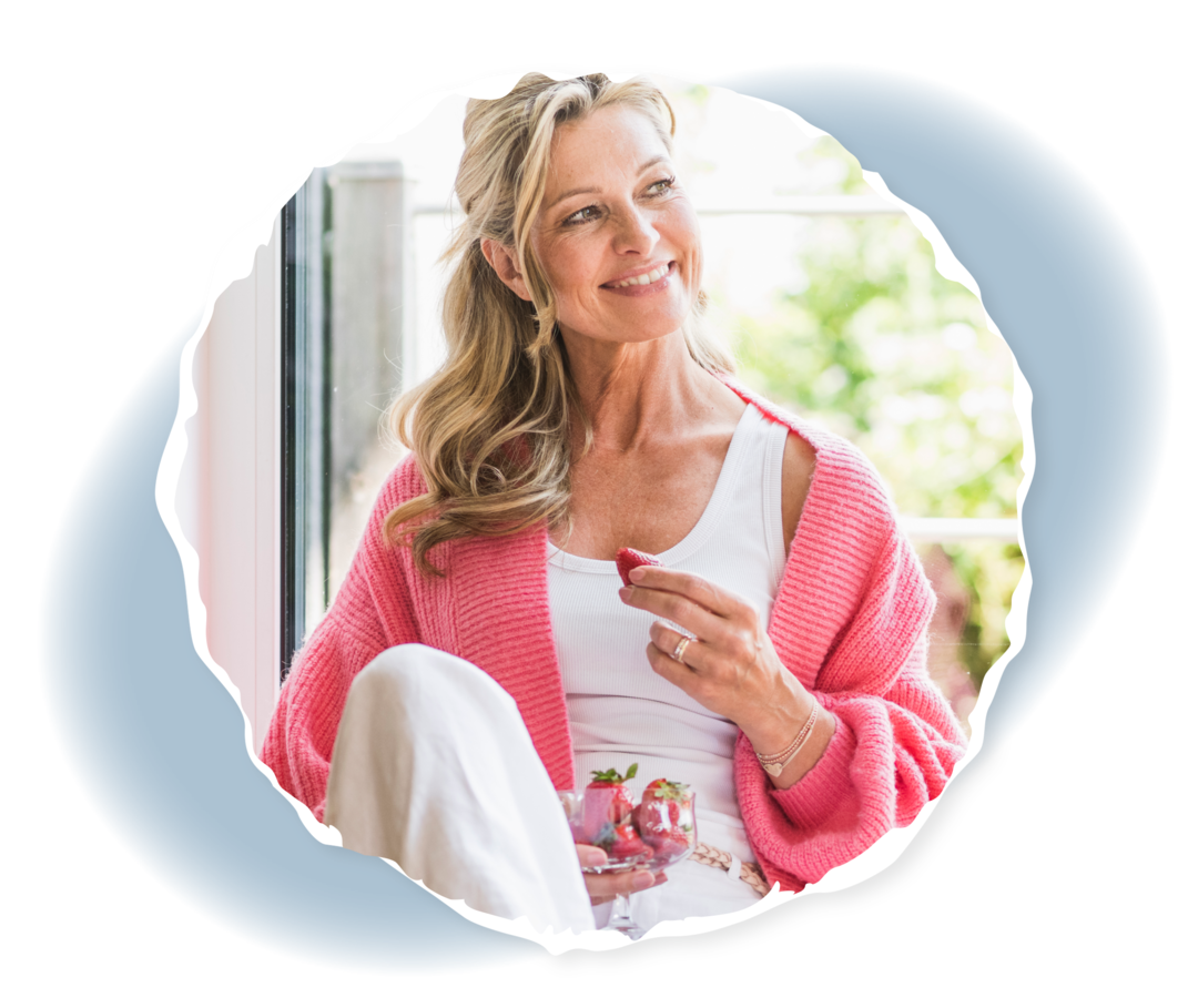 Eine ältere Frau lächelt und hält eine Erdbeere in der Hand.