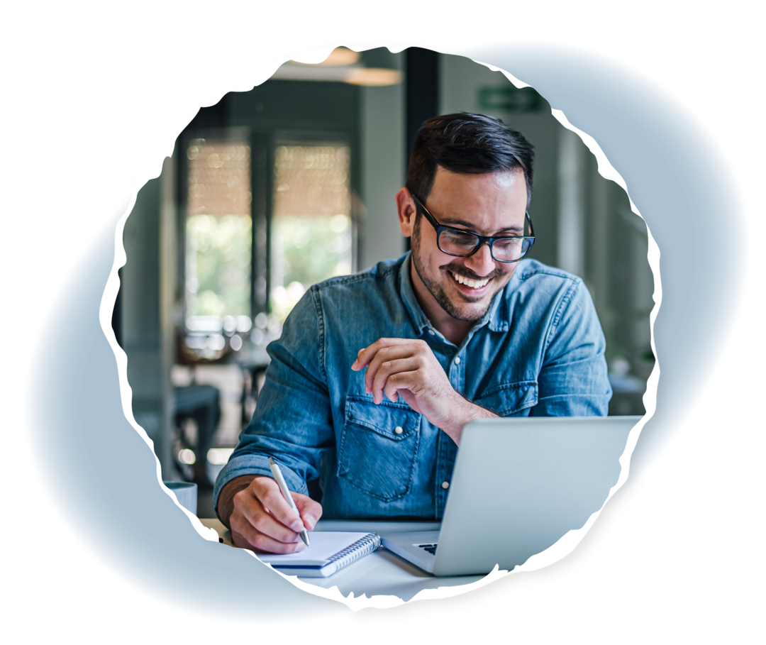 Ein Mann sitzt vor einem Laptop und hält einen Stift in seiner Hand.