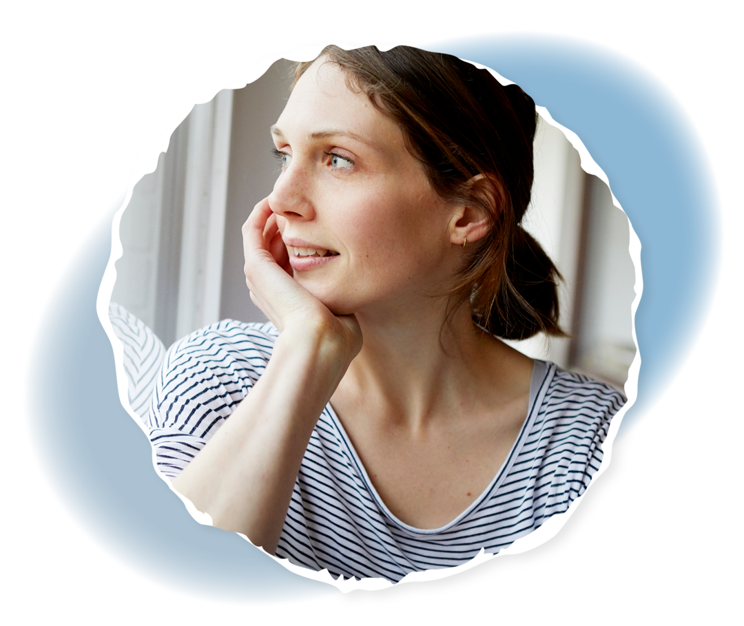 Eine junge Frau sieht aus dem Fenster und lächelt. 