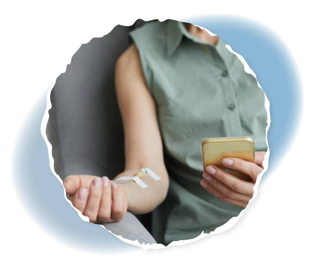 Oberkörper einer Person, die eine Infusion erhält und ein Smartphone in der Hand hält.