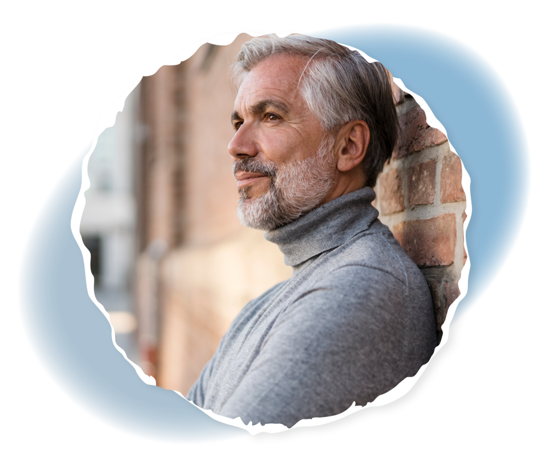 Ein älterer Mann lehnt an einer Mauer und lächelt.