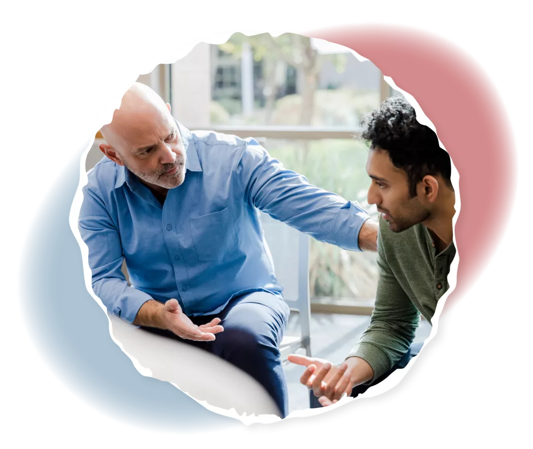 Ein älterer Mann fasst einem jüngeren Mann auf die Schulter und schaut ihn an.