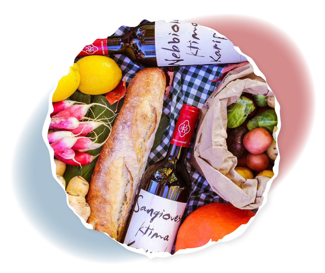 Brot, Obst, Gemüse und Wein auf einer Decke.