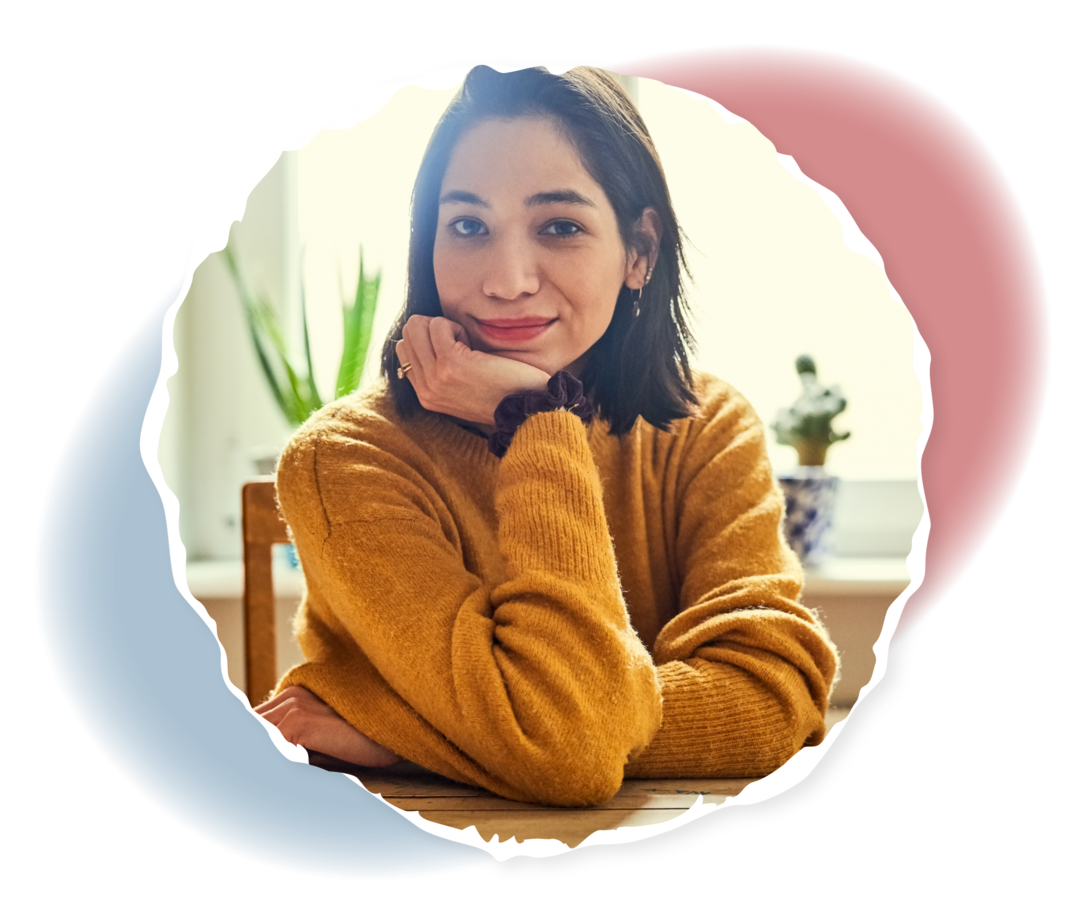 Eine Frau sitzt an einem Tisch und schaut in die Kamera.