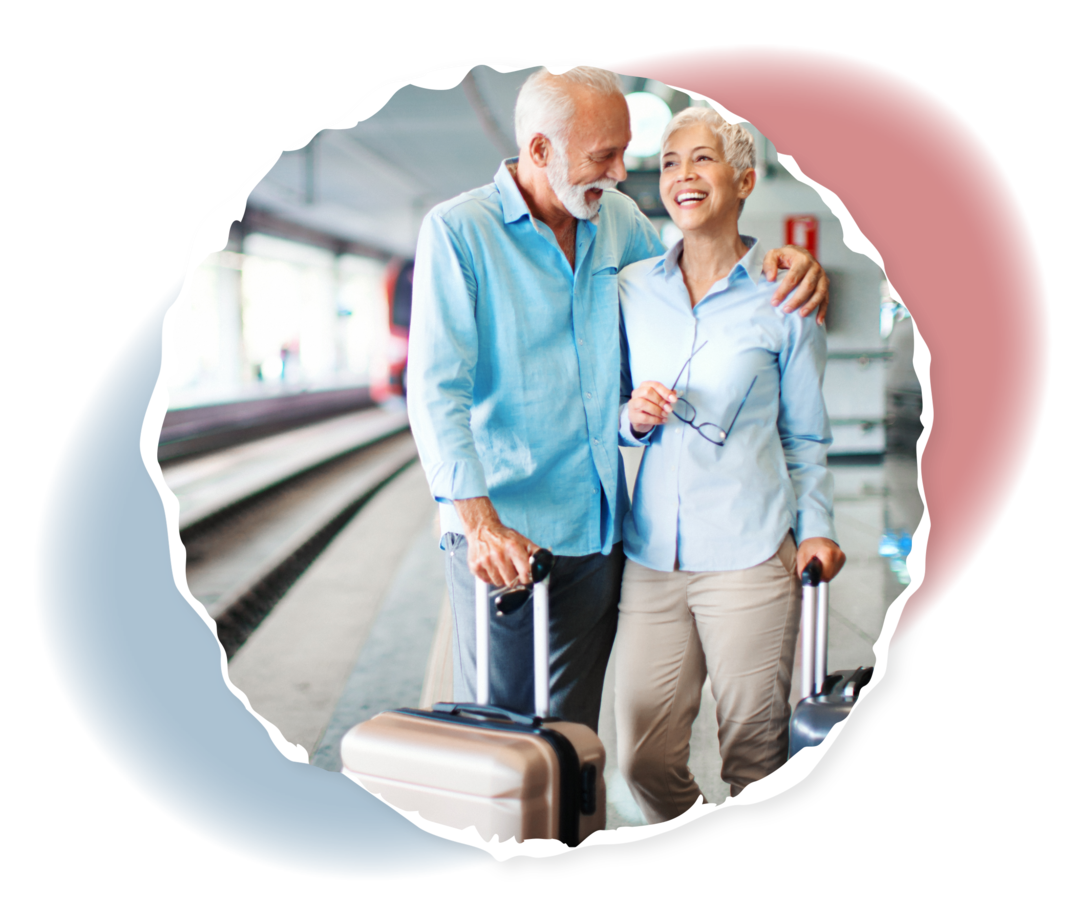 Ein älterer Mann und eine ältere Frau stehen mit zwei Koffern an einem Bahnsteig.