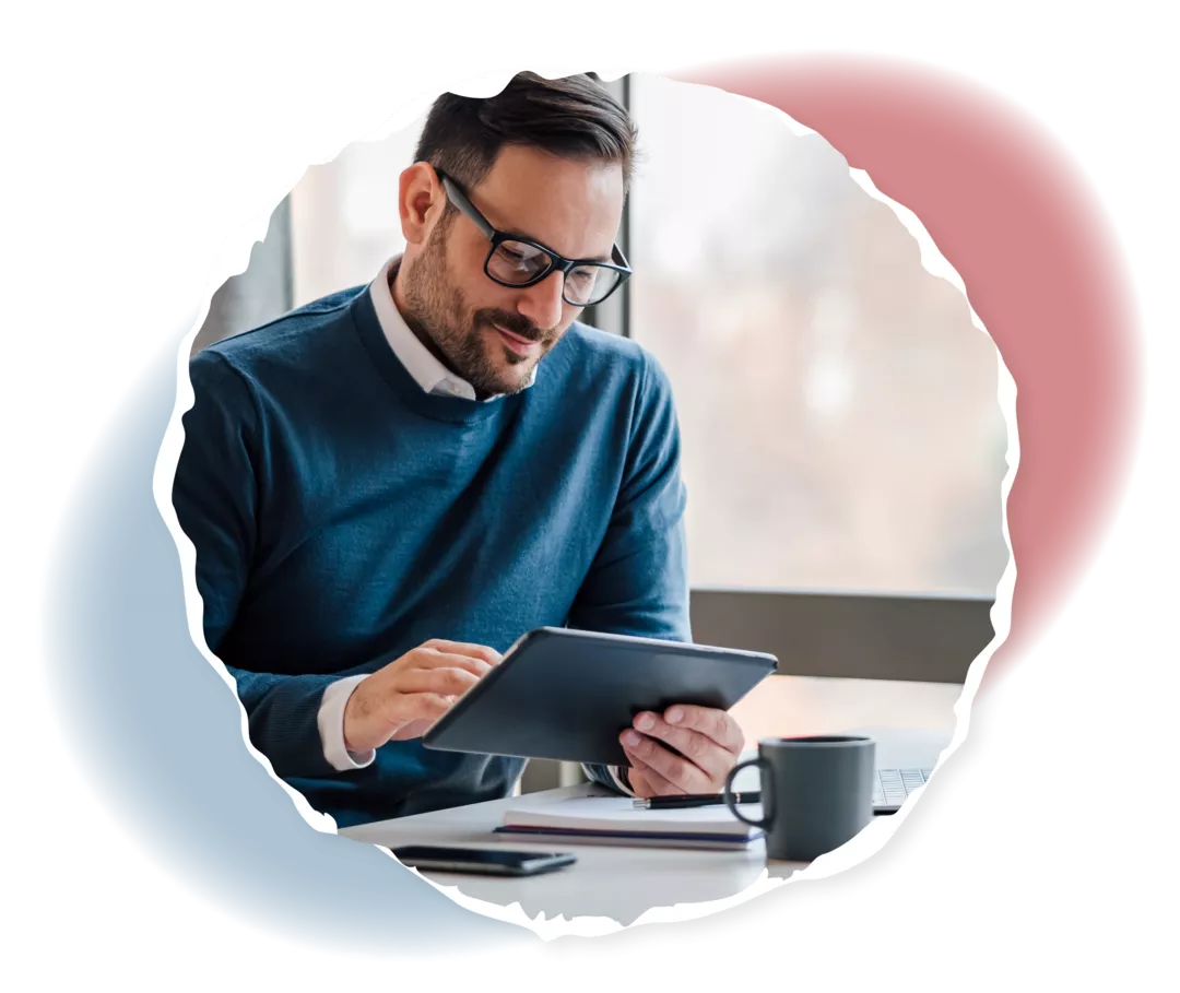 Ein Mann sitzt an einem Schreibtisch und schaut auf ein Tablet.