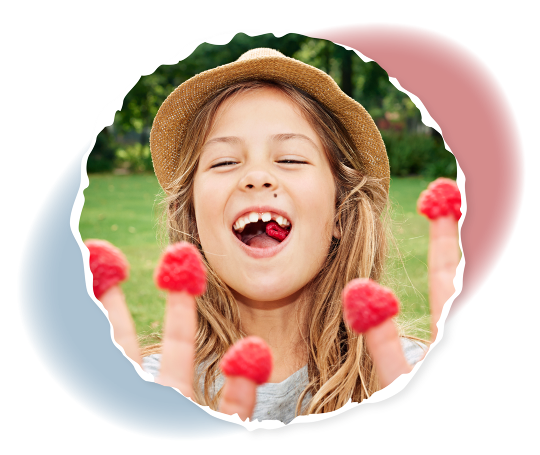 Ein Mädchen hat Himbeeren auf die Fingerspitzen gesteckt und lacht.
