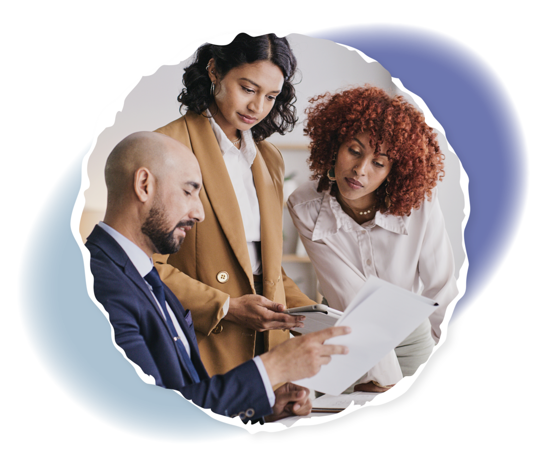 Ein Mann und zwei Frauen schauen sich Unterlagen an einem Schreibtisch an.