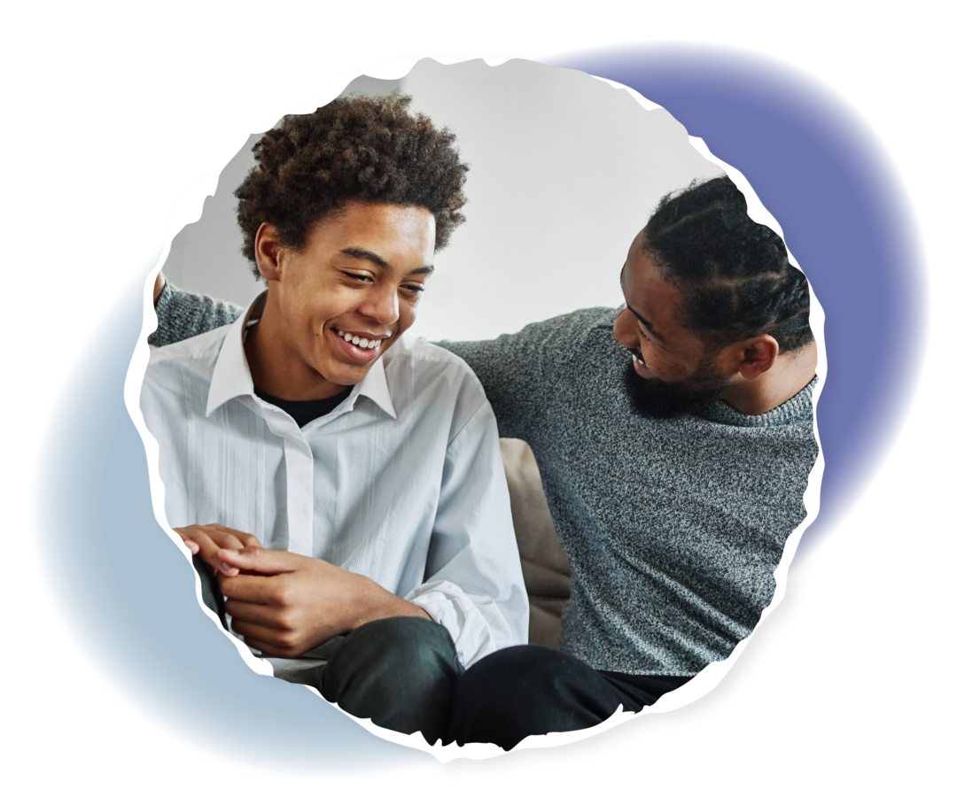 Ein Mann und ein Jugendlicher sitzen auf einem Sofa und lächeln. 