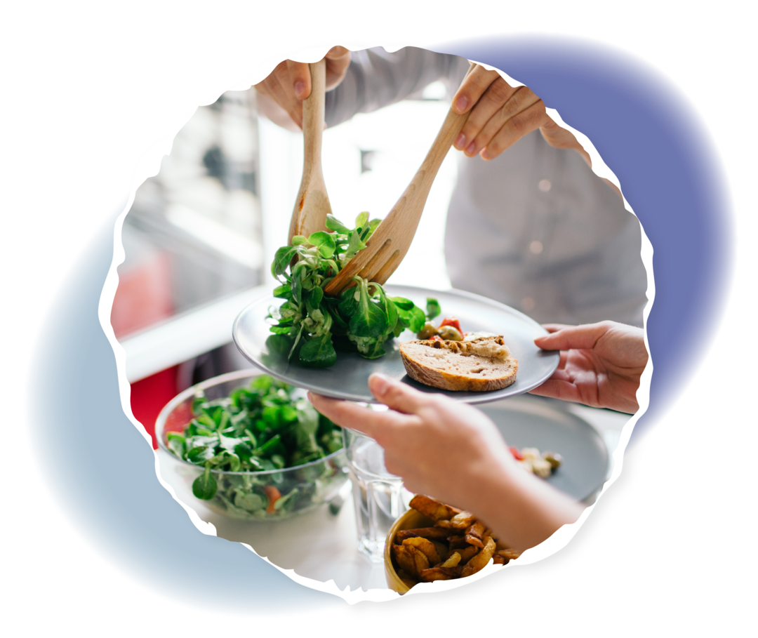 Ein Mann hält zwei Holzlöffel und legt Salat auf einen Teller ab.