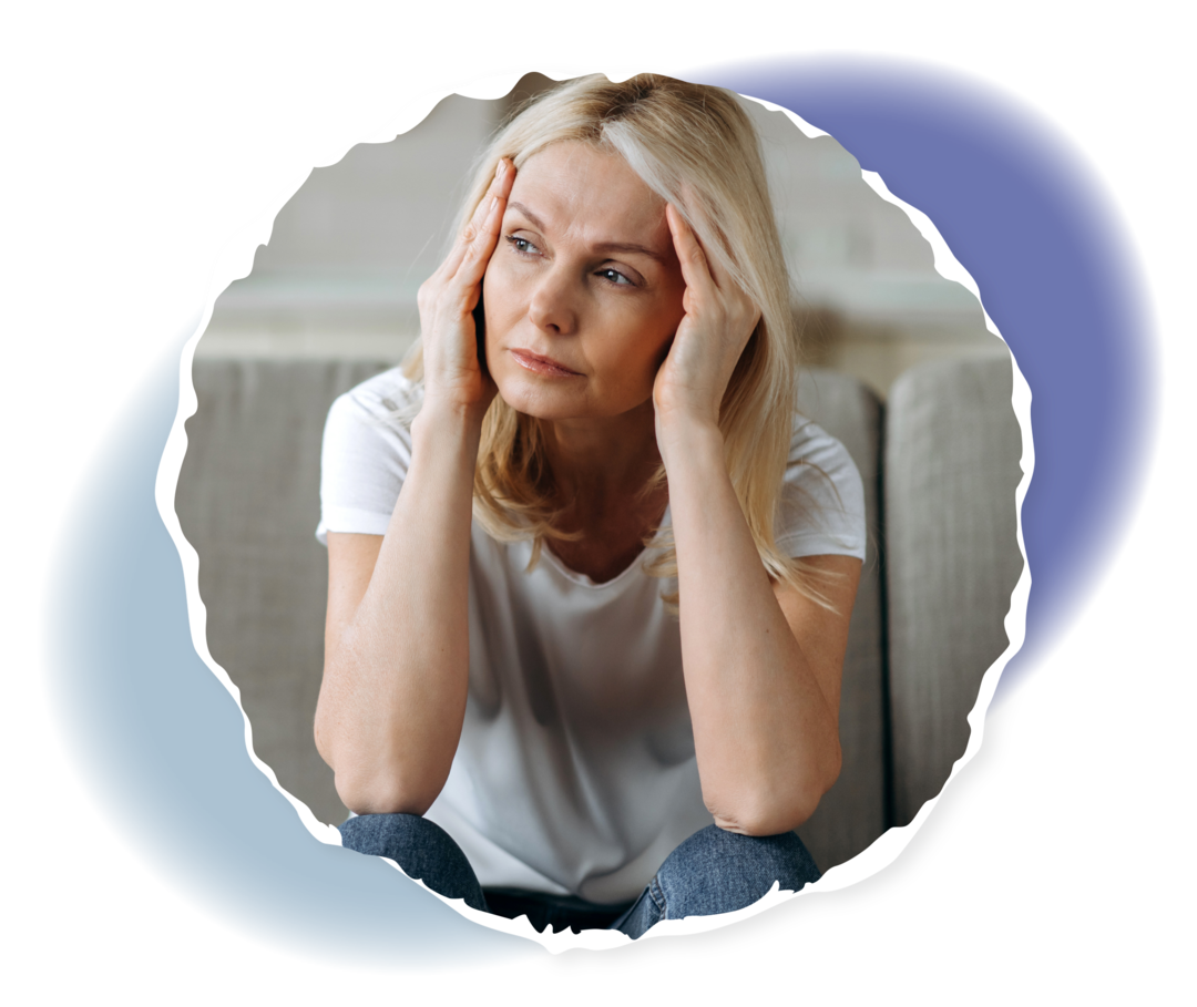 PNH: Fatigue Eine Person sitzt auf einem Sofa und hält sich beide Hände an die Schläfen.