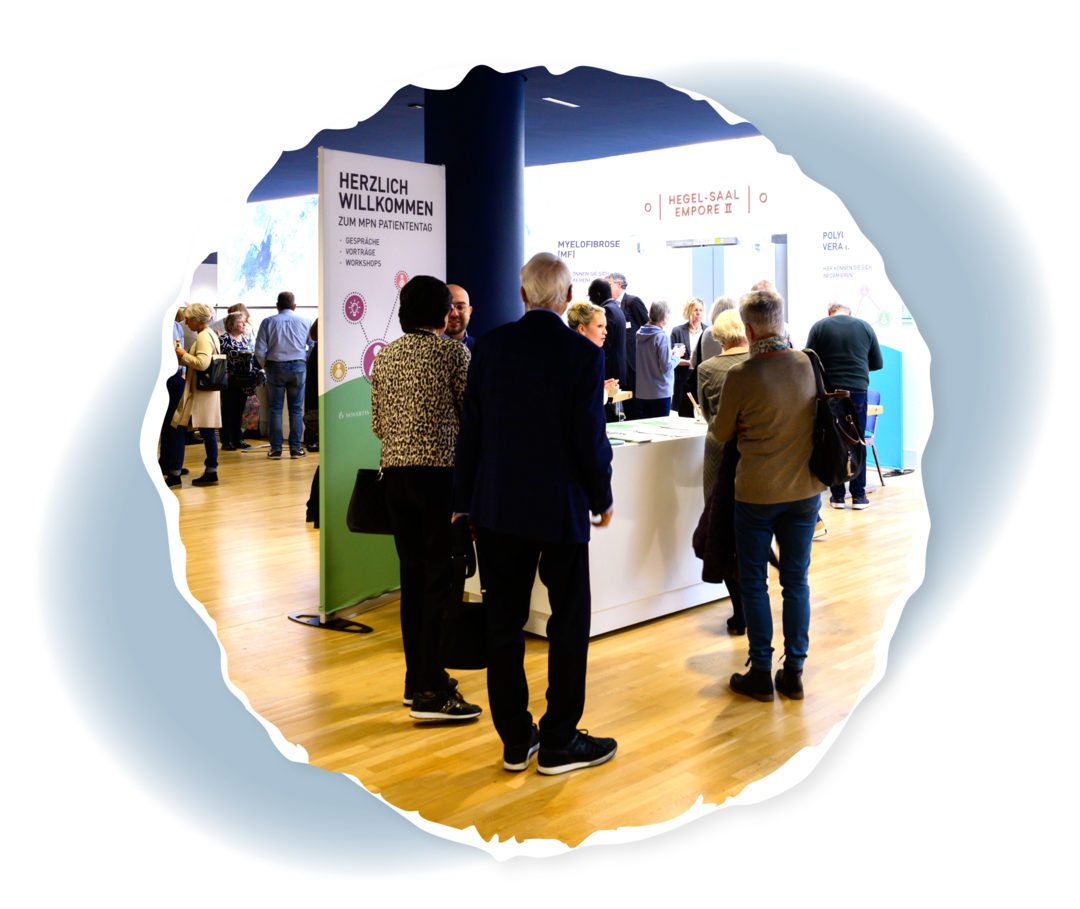 Blick auf den Empfang. Im Hintergrund sind Infostände zusehen. Außerdem weitere Personen im Gespräch.