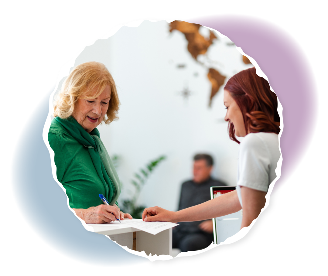 Eine ältere Frau steht einer Rezeption und unterzeichnet ein Schriftstück, das ihr eine Frau in weißem Kittel hinhält.